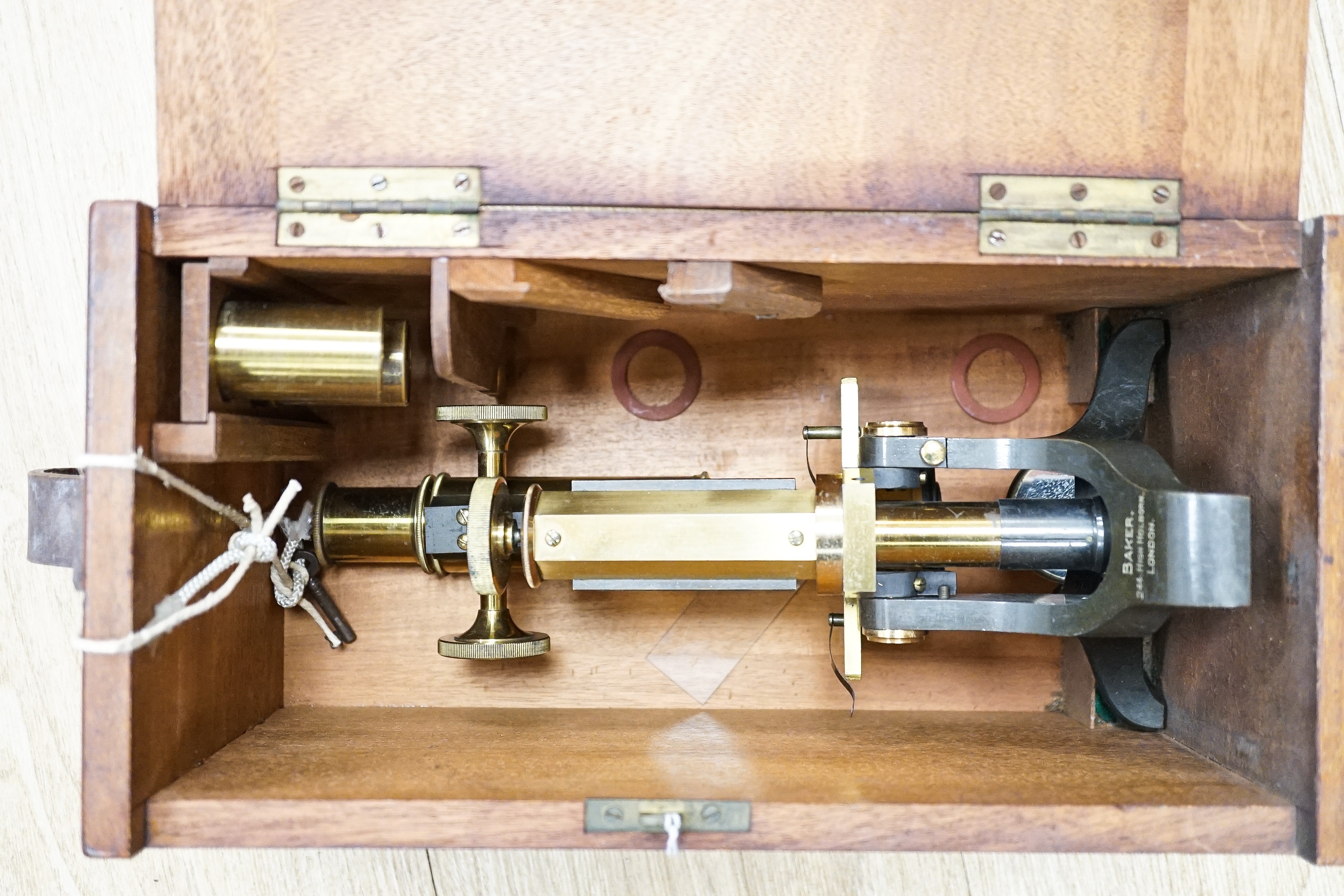 A Baker High Holborn London brass monocular microscope and another brass microscope, both boxed with accessories, largest 43cms wide.